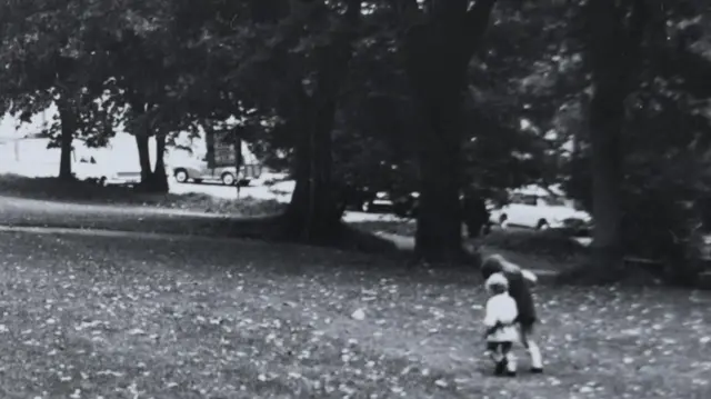 Uma foto em preto e branco de duas crianças pequenas de mãos dadas caminhando em um parque