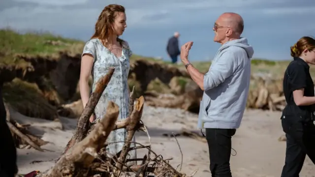 El director de “28 años después”, Danny Boyle, le da indicaciones a Jodie Comer en lo que parece ser una playa. 
