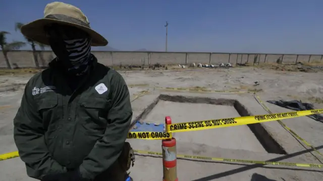 Agente verifica uma possível vala comum, cercada por fita amarela