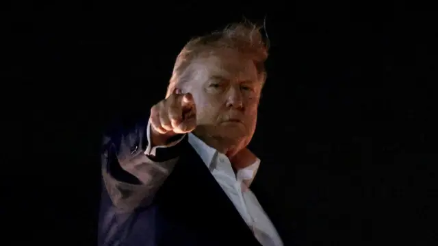 Дональд Трамп в темноте указывает пальцем вперед.