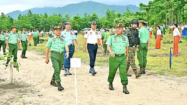 တပ်ချုပ်နဲ့ ဒုချုပ်ကို သစ်ပင်စိုက်ပျိုးပွဲမှာတွေ့ရပြီး တခြားစစ်သည်တွေလည်းရှိနေပါတယ်။ အနောက်မှာတော့ ရှမ်းရိုးမတောင်တန်းတွေကို မြင်နေရပါတယ်။