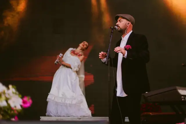 Гурт ADAM під час виступу, Клименко перед мікрофоном, на задньому тлі жінка в довгій білій сукні