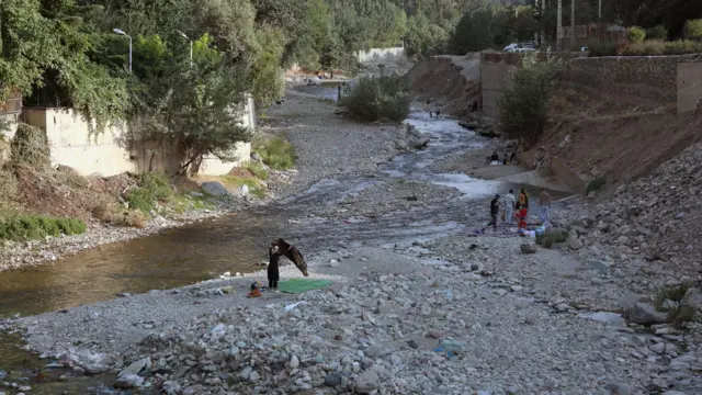 फ़शम में सूखी हुई नदी की तलहटी पर मौजूद ईरानी लोग