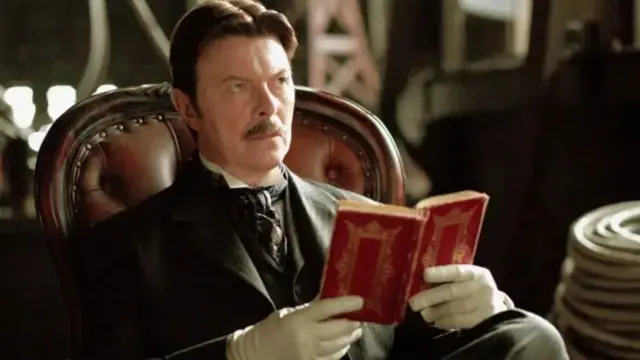 Dejvid Bouvi sa brkovima u odelu drži crvenu knjigu