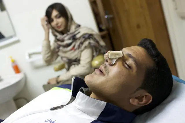 Wani mutum da aka yi wa aikin gyaran fuska, kwance a gaban wata mata