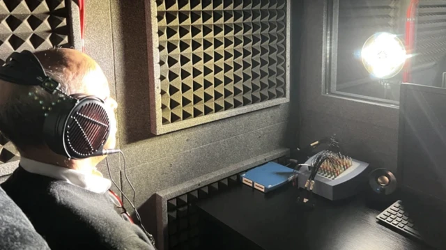 مردی در یک اتاق آزمایش نشسته گوشی دارد و نوری از مقابل به چشمهایش می تابد