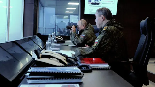 Путин смотрит в бинокль на учениях в Ростове-на-Дону. Рядом с ним сидит начальник Генштаба Герасимов