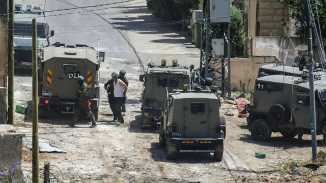 صورة تُظهر جنودا إسرائيليين يقفون قرب سيارات عسكرية ويقومون بتكبيل فلسطيني في الضفة الغربية