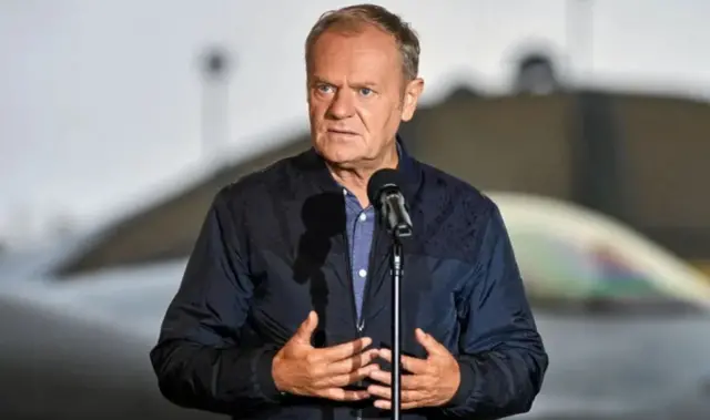 Дональд Туск дивиться прямо перед мікрофоном у синій куртці