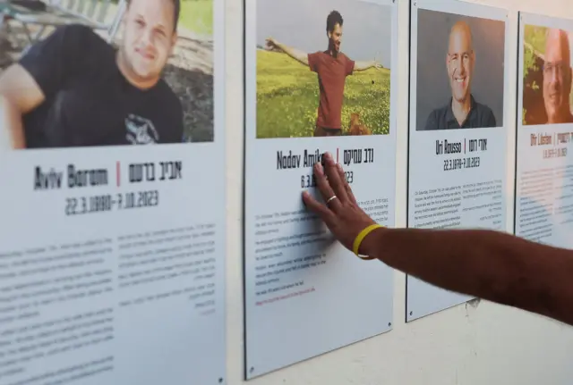 вытянутая рука касается портрета молодого мужчины с биографией, он один из жертв нападения ХАМАС в кибуце Кфар-Аза