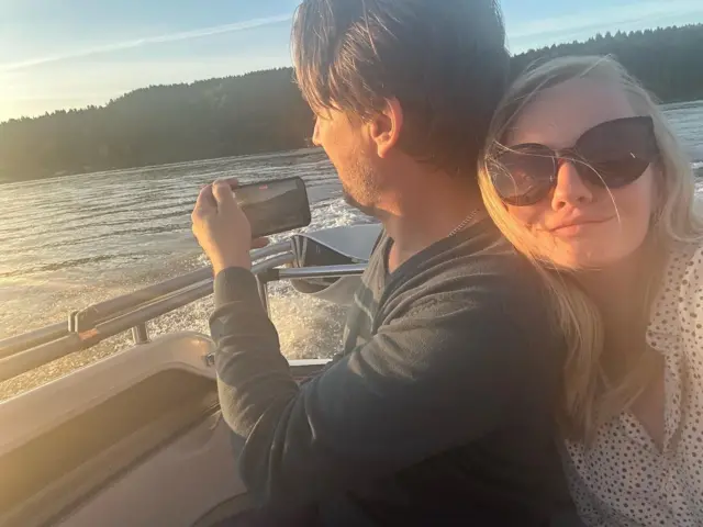 Девушка в темных очках и мужчина с мобильным телефоном на катере посредине реки