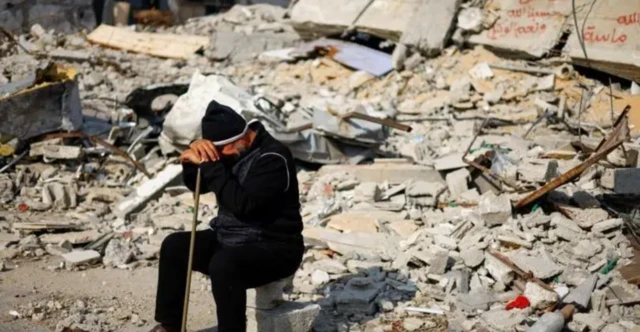 Homem sentado a meio escombros de área destruída em Gaza