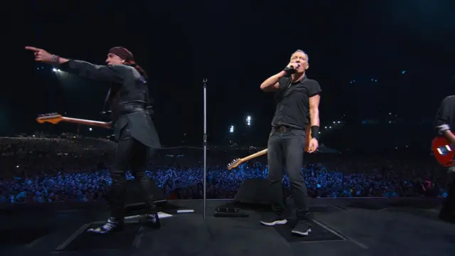 Brus Springstin (na desnoj strani) i Stiv van Zant na bini tokom svetske turneje, obojica nose crnu odeću i drže gitare. Van Zant gleda u publiku i pokazuje prstom dok Springstin gleda ka zadnjem delu bine.