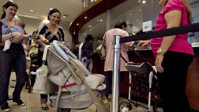 kolica za bebe ispred bioskopske blagajne, jedna žena drži bebu u nosiljci