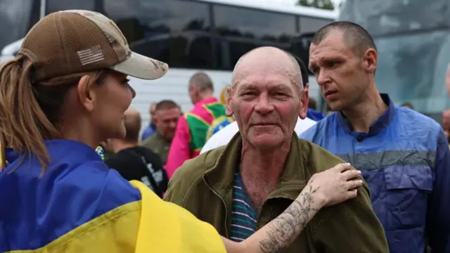 Укрнаинский военный и девушка с украинским флагом на плечах, на заднем плане еще один военный
