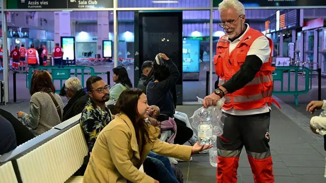 متطوع من الصليب الأحمر يوزع الماء على المنتظرين في محطة قطار خواكين سورولا، في فالنسيا، في 28 أبريل/نيسان 2025، بعد انقطاعٍ شامل للتيار الكهربائي شمل شبه الجزيرة الأيبيرية وجنوب فرنسا. 