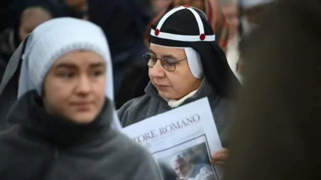 One nun read newspaper di Osservatore Romano Catholic newspaper as she wait for di funeral Mass to start