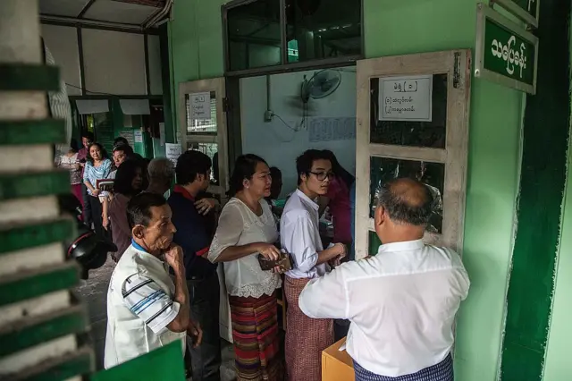 သပြေခန်းလို့ နာမည်ပေးထားတဲ့ အစိမ်းရောင်စာသင်ခန်းရှေ့မှာ တန်းစီနေကြသူတွေ 