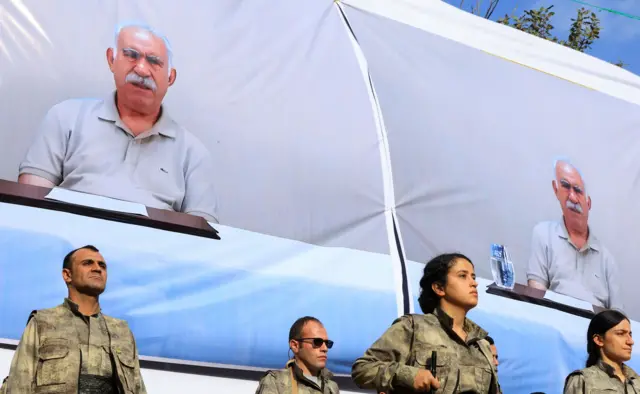 PKK militanları, Türkiye ile yasadışı örgüt arasında onlarca yıldır süren çatışmayı sona erdirmeye yönelik Irak’taki Kandil Dağları’nda düzenlenen bir silahsızlanma töreni sırasında Öcalan fotoğrafı önündeler. 26 Ekim 2025.