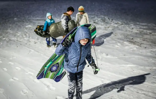 சாலைகளில் உறைந்து கிடக்கும் பனியில் ஆர்வத்துடன் சறுக்கி விளையாடச் செல்லும் குழந்தைகள்