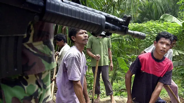 Seorang tentara mengawasi warga sipil yang direkrut oleh militer Indonesia untuk memperbaiki jalan yang rusak selama pertempuran antara pasukan pemerintah dan gerilyawan GAM, Peusangan, Aceh Utara, 24 Mei 2003.