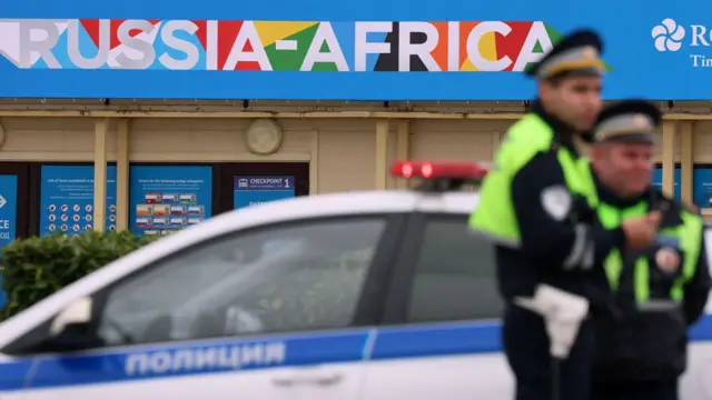 Deux officiers de la police routière montent la garde près d'une voiture de police sur le bord d'une route, avec la marque du sommet Russie-Afrique derrière eux, à Sochi, Russie - 8 novembre 2024.