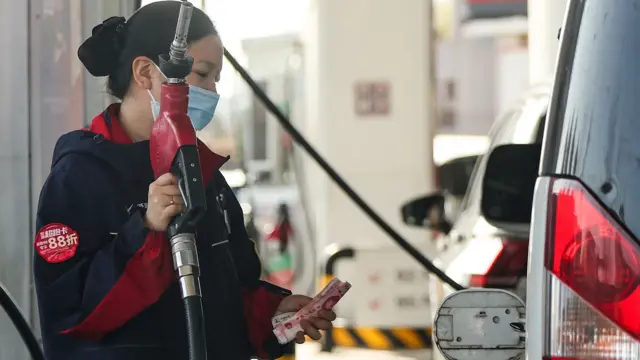 一名員工在中國北京一個加油站為汽車加油時，手持油槍和人民幣鈔票（22/3/2026）