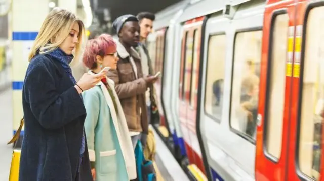 मेट्रो में अपना फोन देखते हुए लोग