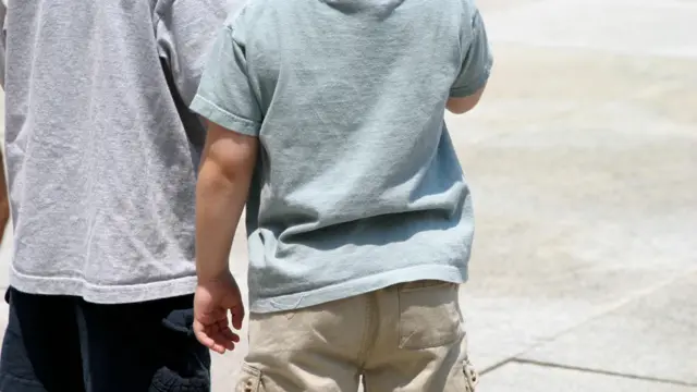 एकमेकांच्या शेजारी उभ्या असलेल्या दोन लहान मुलांचे मागून घेतलेले फोटो.