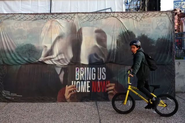 طفل يقود درّاجة هوائية مروراً بلافتة مخصّصة للرهائن منذ هجوم السابع من أكتوبر/تشرين الأول.