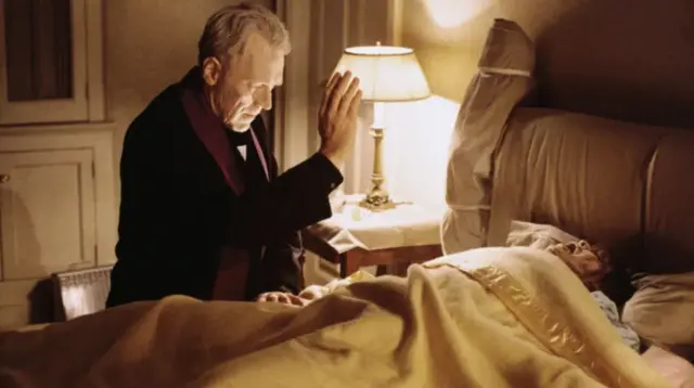 Cena de 'O Exorcista' retratando padre Merrin (Max von Sydow) Max von Sydow fazendo o sinal da cruz junto a Regan (Linda Blair) deitada na cama