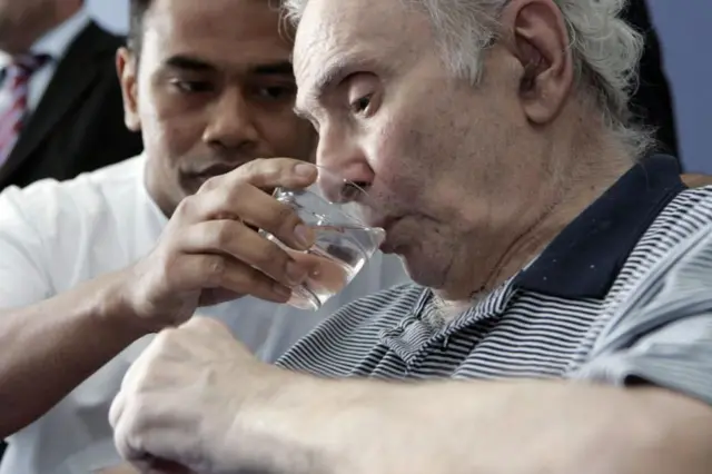 एक परिचारक काळजीपूर्वकपणे एक वृद्ध व्यक्तीला पाणी देताना.