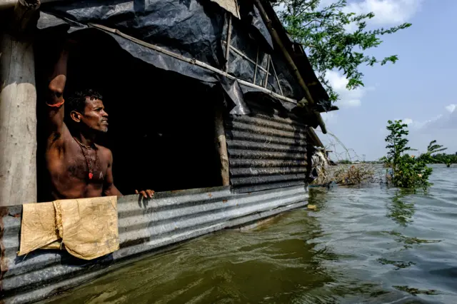 Seorang penduduk desa berdiri di dalam rumahnya yang setengah terendam saat banjir di Sundarban, India