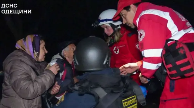 赤い制服に白いヘルメットをかぶった救急隊員が、避難した高齢の男女と話している