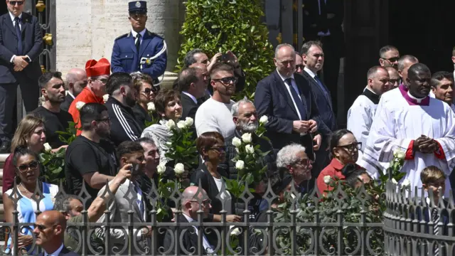Pessoas com rosas brancas aguardam a chegada do caixão do papa Francisco