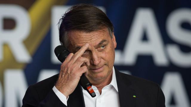 Bolsonaro coçando a testa e segurando microfone