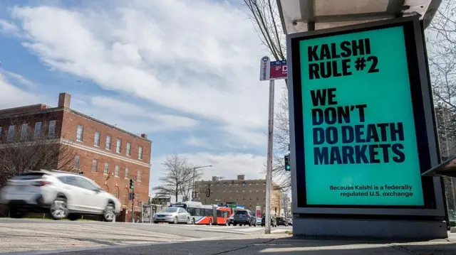 Un cartel de Kalshi en el que dice que la regla número 2 de Kalshi es no participar en mercados de predicción de muertes. A lado circulan autos.  Foto tomada en Washington DC