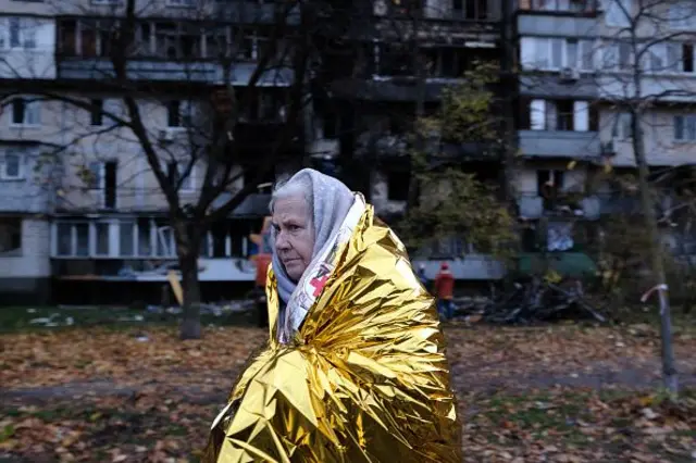 Літня жінка у золотій термічній ковдрі на тлі багатоповерхового будинку