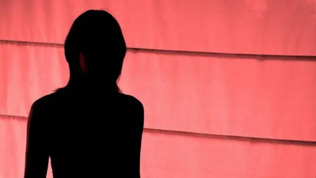 Vulto de mulher em pé, em frente a uma parede vermelha