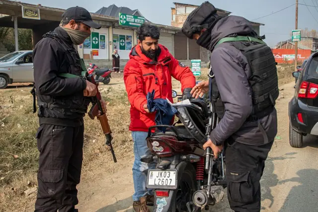 অস্ত্র হাতে দুইজন নিরাপত্তারক্ষী একটি মোটরসাইকেল ও তার আরোহীকে তল্লাশি করছে