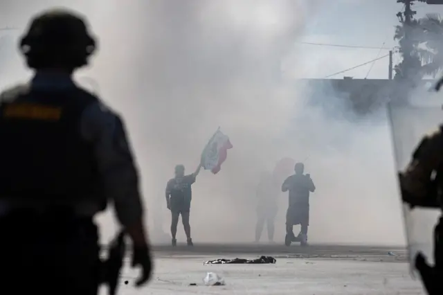Manifestantes cubiertos de humo durante un enfrentamiento con la policía.