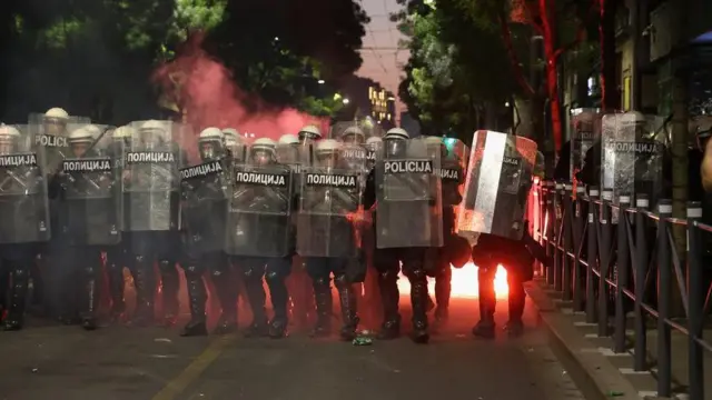 kordon policije sa štitovima, iza njih bačena baklja 