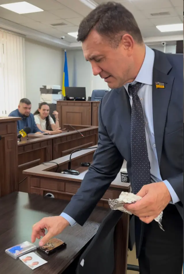 "Ось так буде", – каже журналістам Тищенко, розкладаючи фото своїх дітей та ікону на столі, імітуючи їхню розстановку у камері СІЗО