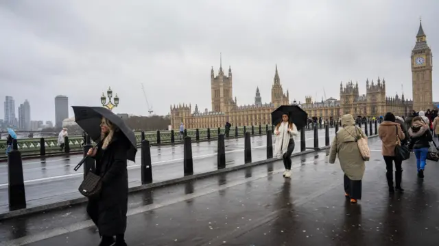 Piesi z parasolami przechodzą przez Most Westminsterski przed Parlamentem podczas sztormu Darragh 7 grudnia 2024 roku w Londynie