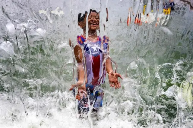 د امریکا په ختیځ ساحل کې د تودوخې څپې په اوږده کې یو هلک د اوبو تر فوارې لاندې لوبې کوي. انځور د اوبو د انعکاس له امله ګډ وډ ښکاري.