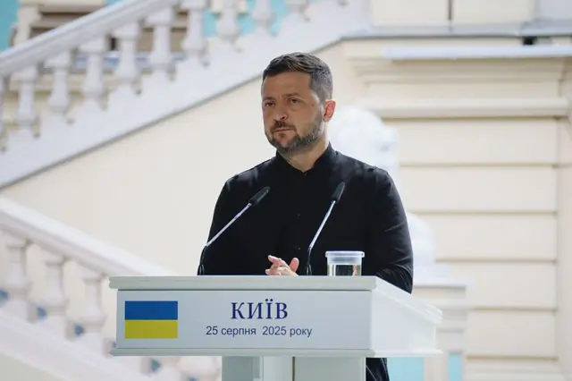 Зеленський у чорній сорочці за мікрофонами, він має серйозний вираз обличчя. На стійці напис "Київ. 25 серпня 2025 року".