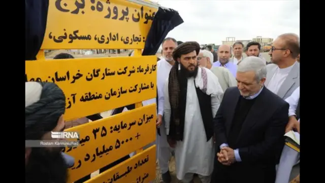  مقامات ایرانی همراه با مقامات حکومت طالبان در بندر چابهار هنگام افتتاح برج فاخر. آنها کنار یک لوحه زرد رنگ ایستاده‌اند که جزئیات پروژه را شرح می‌دهد.