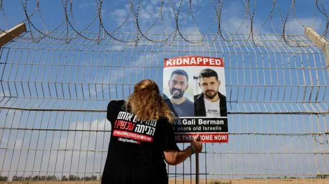 Israeli woman holds poster of Israeli hostages while looking through fence towards Gaza (file photo)