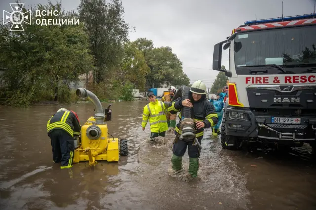 По коліна у воді рятувальники несуть дорогою великий шланг для відкачування води