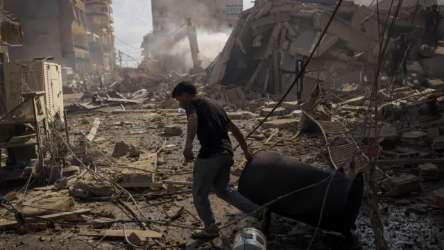 Lübnan'ın Tire kentindeki bir sokaktaki yıkıntıların arasında dolaşan bir adam bir bidon çekiyor